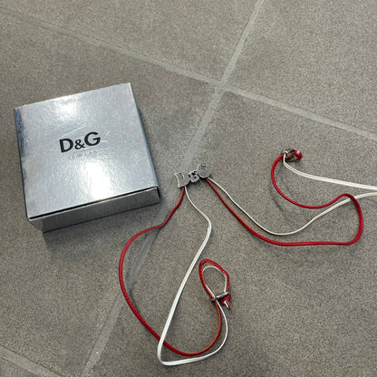 Dolce &amp; Gabbana 2000s Red &amp; White Strings Necklace &amp; Bracelet is a versatile accessory featuring red and white leather cords joined with stainless steel end caps. The center is finished with a stainless steel D&amp;G logo, while the back of the logo features a small engraved D&amp;G mark. Designed to be worn either as a necklace or wrapped as a bracelet, it comes complete with its original box.