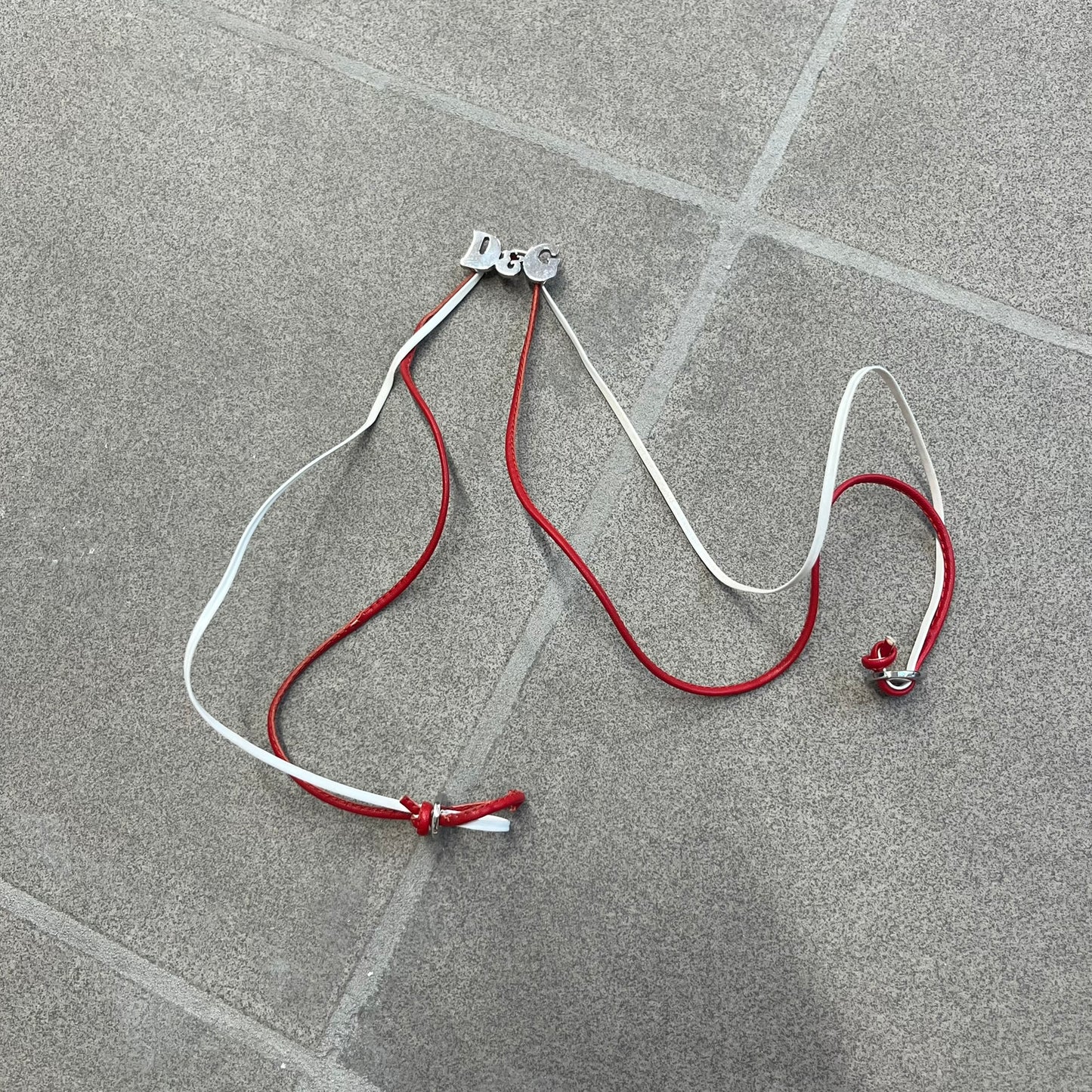 Dolce &amp; Gabbana 2000s Red &amp; White Strings Necklace &amp; Bracelet is a versatile accessory featuring red and white leather cords joined with stainless steel end caps. The center is finished with a stainless steel D&amp;G logo, while the back of the logo features a small engraved D&amp;G mark. Designed to be worn either as a necklace or wrapped as a bracelet, it comes complete with its original box.