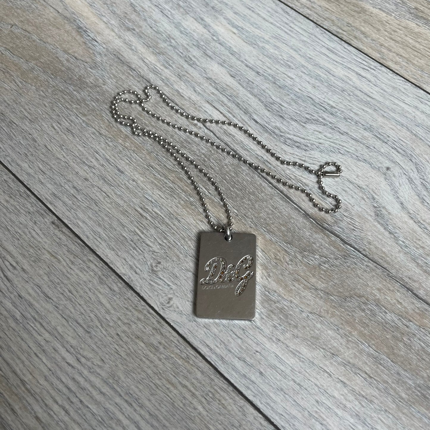 Dolce &amp; Gabbana Rhinestones Dog Tag Necklace DJ0704 crafted from polished stainless steel. Features a rectangular pendant with the iconic D&amp;G logo detailed in rhinestones, and “Dolce &amp; Gabbana” engraved subtly below. Comes with a basic non-D&amp;G steel ball chain.