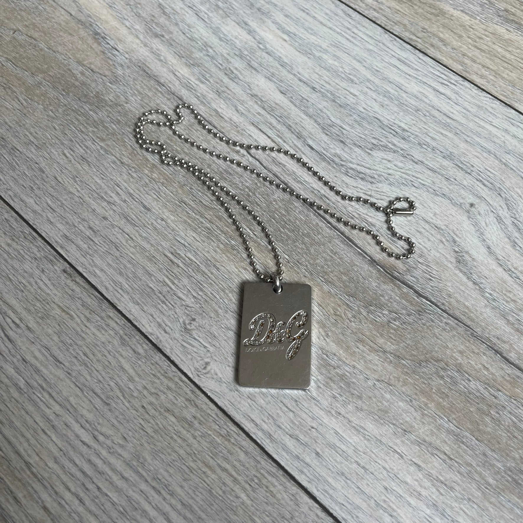 Dolce &amp; Gabbana Rhinestones Dog Tag Necklace DJ0704 crafted from polished stainless steel. Features a rectangular pendant with the iconic D&amp;G logo detailed in rhinestones, and “Dolce &amp; Gabbana” engraved subtly below. Comes with a basic non-D&amp;G steel ball chain.