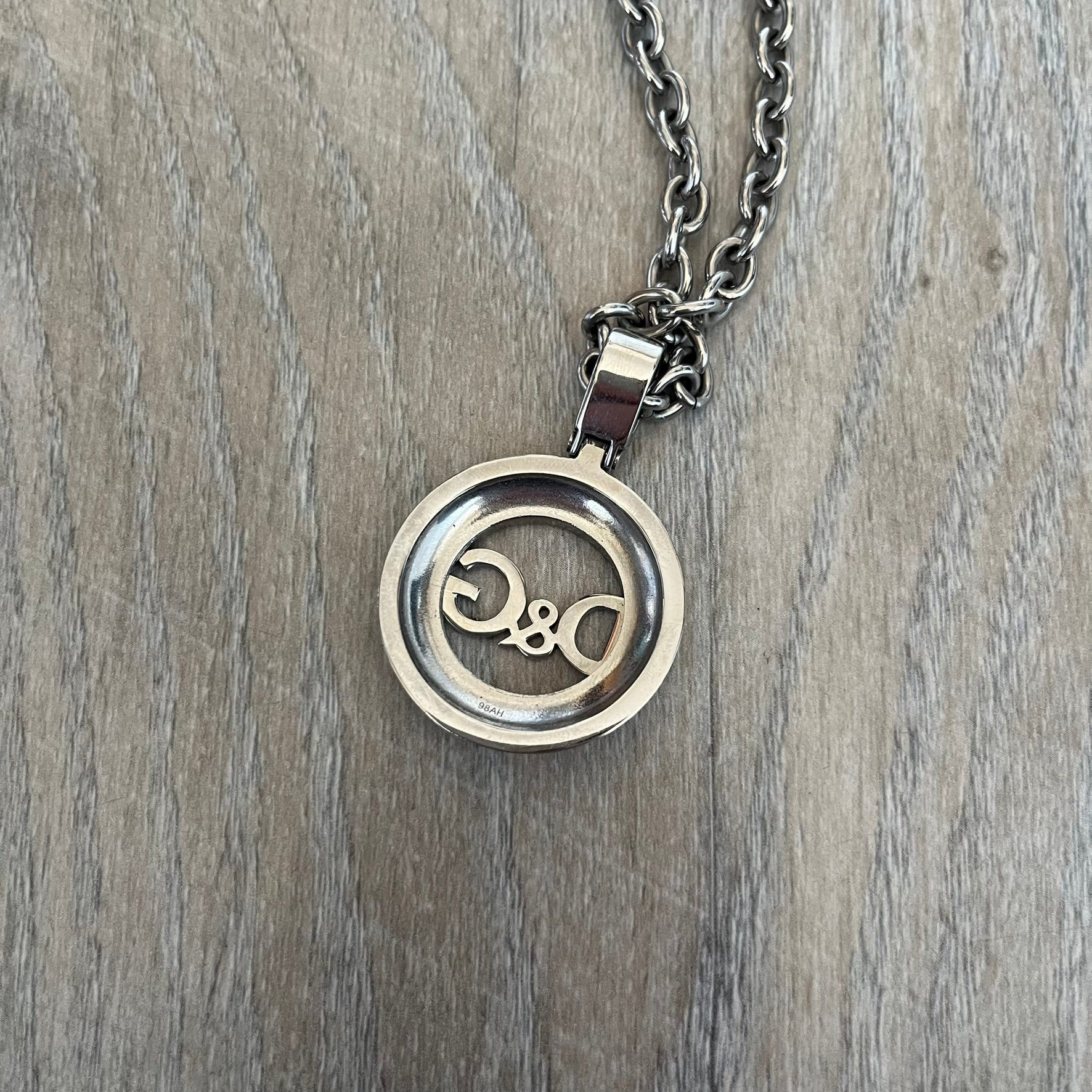 Dolce & Gabbana 2000s Round D&G Logo Necklace is a chain necklace featuring a lobster clasp closure and a thick 3D circular pendant with cut-out center and D&G logo in the middle. The pendant connector is embellished with crystal detailing. The necklace comes with a brown Dolce & Gabbana dust bag.