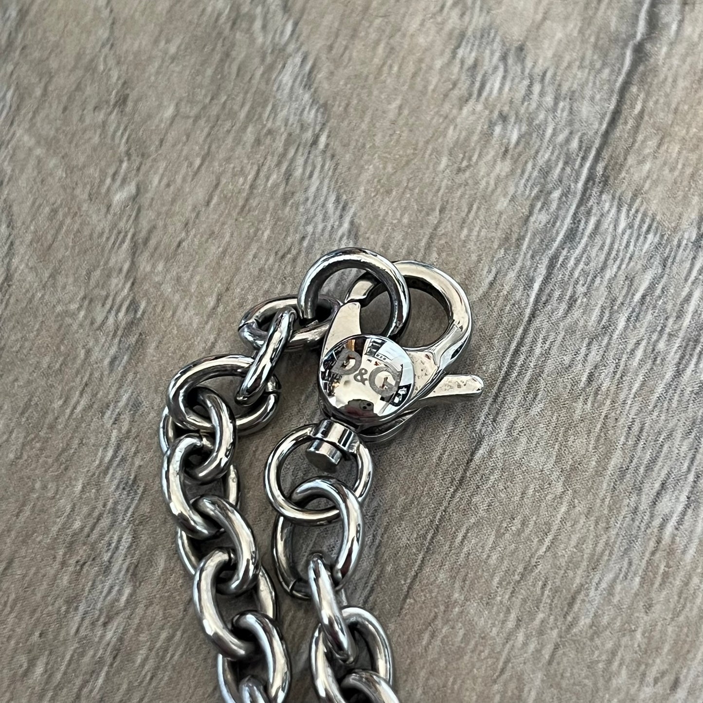 Dolce & Gabbana 2000s Round D&G Logo Necklace is a chain necklace featuring a lobster clasp closure and a thick 3D circular pendant with cut-out center and D&G logo in the middle. The pendant connector is embellished with crystal detailing. The necklace comes with a brown Dolce & Gabbana dust bag.