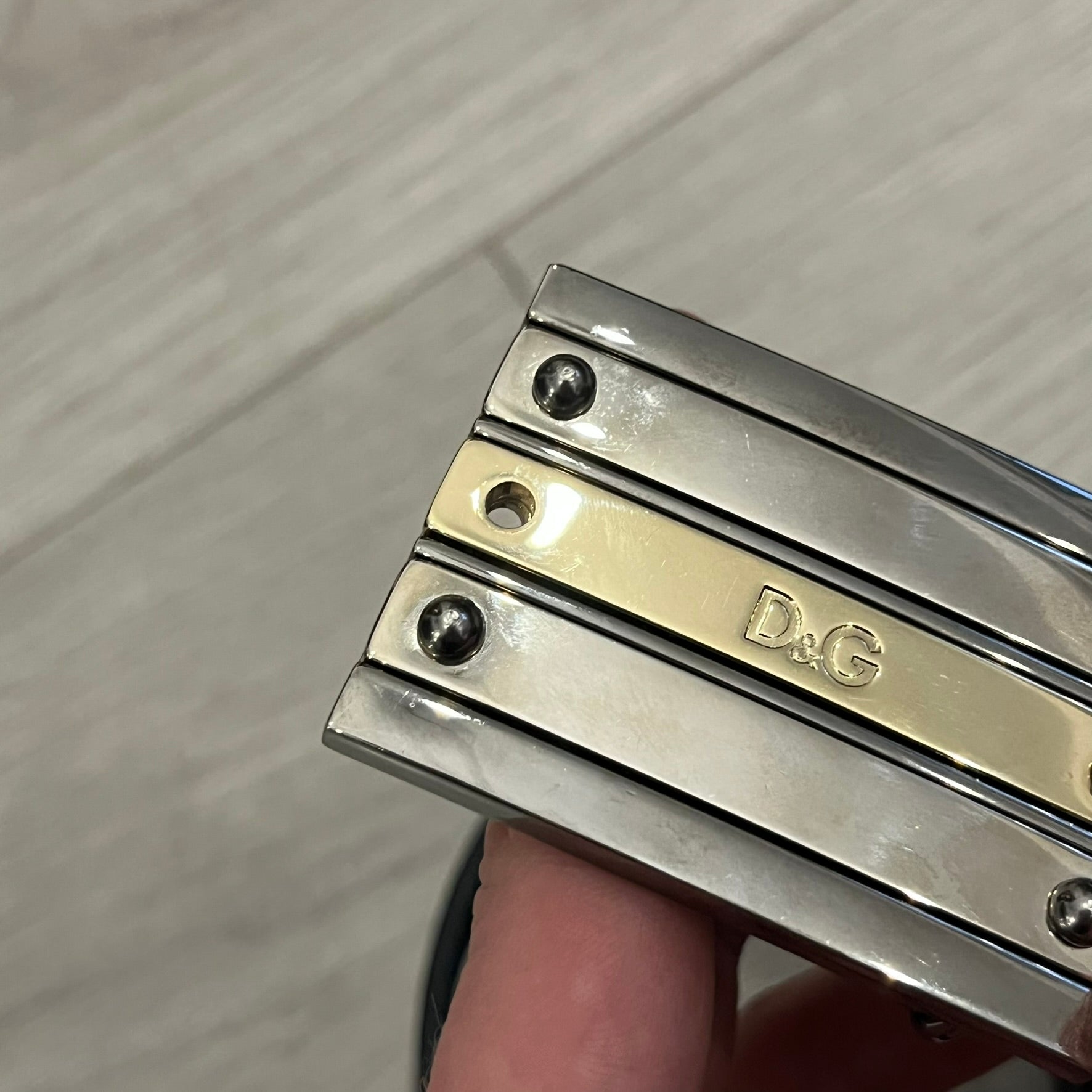 Dolce &amp; Gabbana 2000s Silver/Gold Bars Belt crafted from black leather with a solid metal buckle plate. The buckle features three horizontal metal bars secured with visible screws, with silver-tone bars on the top and bottom and a gold-tone center bar engraved with the D&amp;G logo. Finished with a structured leather strap, comes with the original dustbag.
