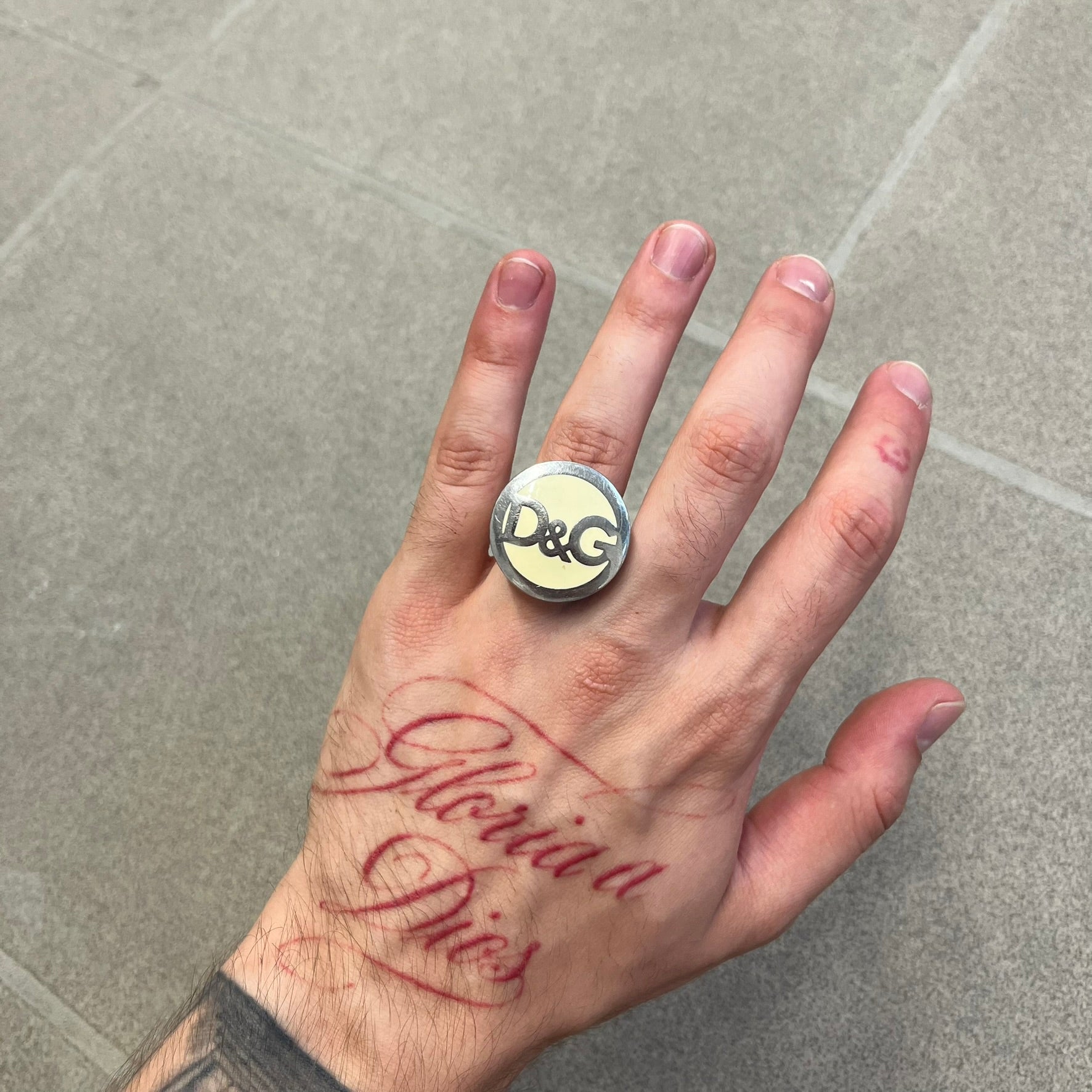 The Dolce &amp; Gabbana Silver Logo Signet Ring is a silver-tone metal signet ring with a thick, substantial design. The top features a beige background with the D&amp;G logo in silver tone, outlined in silver. The signet is large and solid.