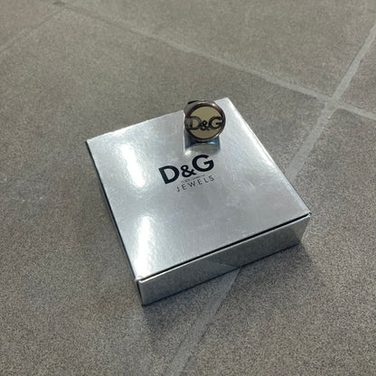 The Dolce &amp; Gabbana Silver Logo Signet Ring is a silver-tone metal signet ring with a thick, substantial design. The top features a beige background with the D&amp;G logo in silver tone, outlined in silver. The signet is large and solid.