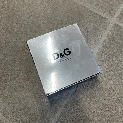 The Dolce &amp; Gabbana Silver Logo Signet Ring is a silver-tone metal signet ring with a thick, substantial design. The top features a beige background with the D&amp;G logo in silver tone, outlined in silver. The signet is large and solid.