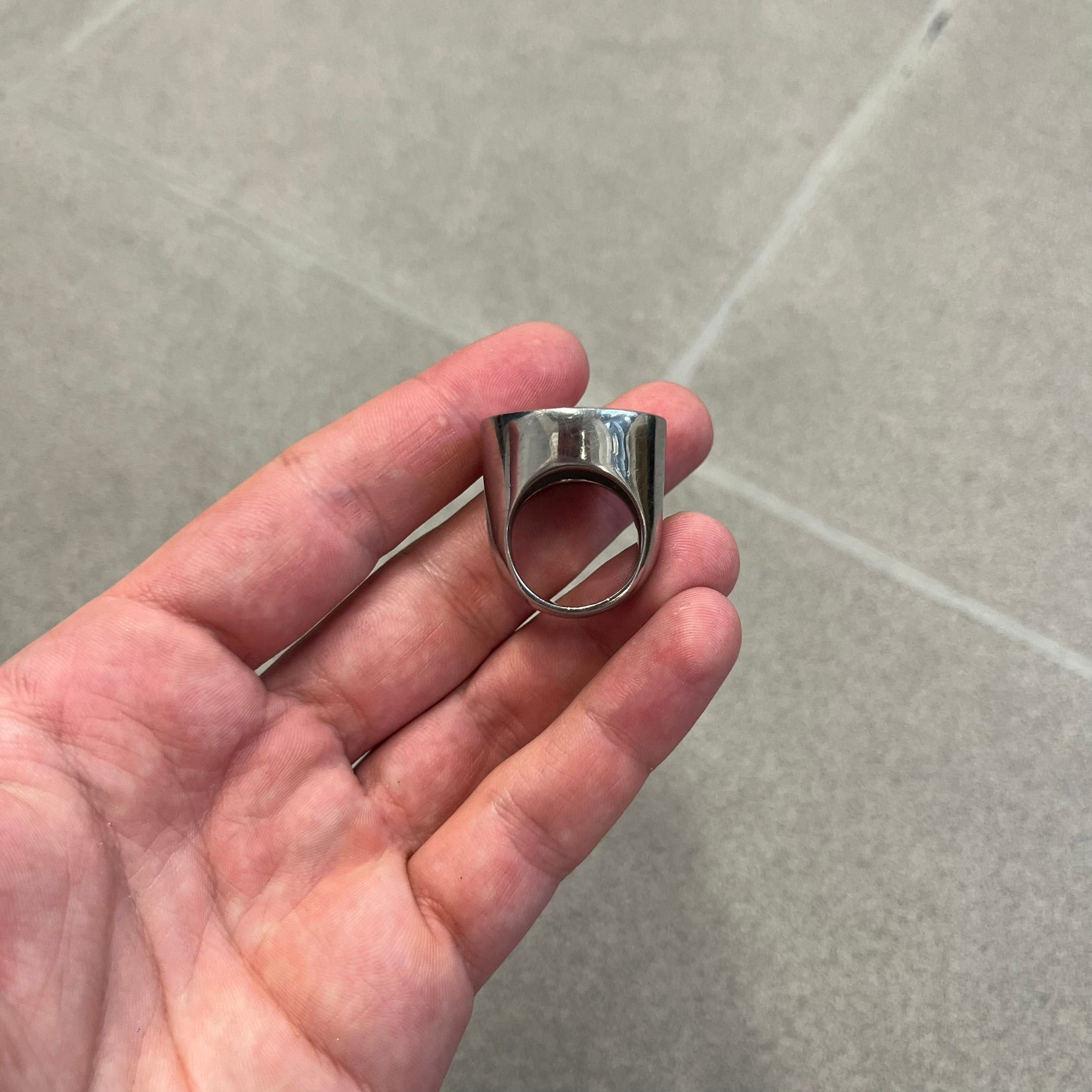 The Dolce &amp; Gabbana Silver Logo Signet Ring is a silver-tone metal signet ring with a thick, substantial design. The top features a beige background with the D&amp;G logo in silver tone, outlined in silver. The signet is large and solid.