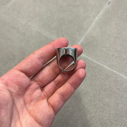 The Dolce &amp; Gabbana Silver Logo Signet Ring is a silver-tone metal signet ring with a thick, substantial design. The top features a beige background with the D&amp;G logo in silver tone, outlined in silver. The signet is large and solid.