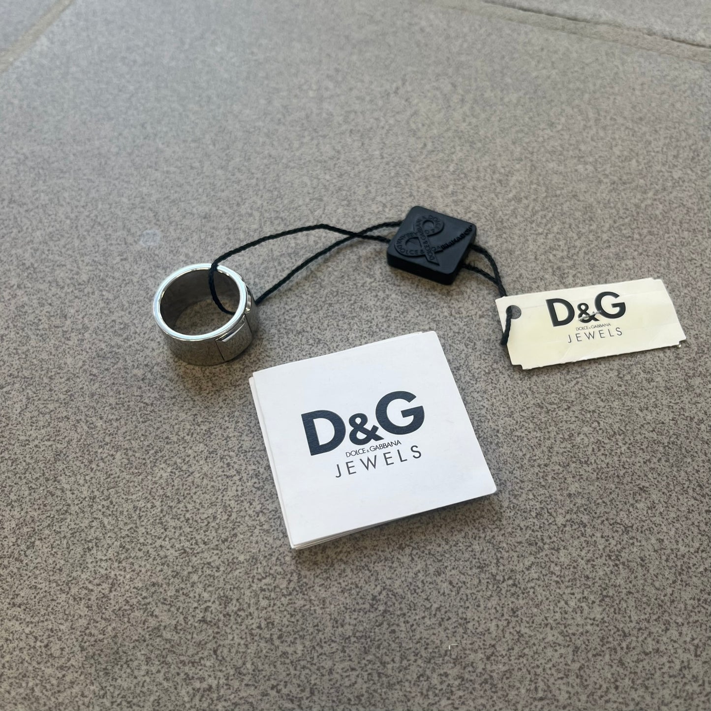 Dolce &amp; Gabbana DJ0836 Ring is made from silver-tone metal and features three raised square elements set across the top. Next to the squares, there is a small engraved D&amp;G logo. The ring has a clean, minimal design and is marked with model code DJ0836.
