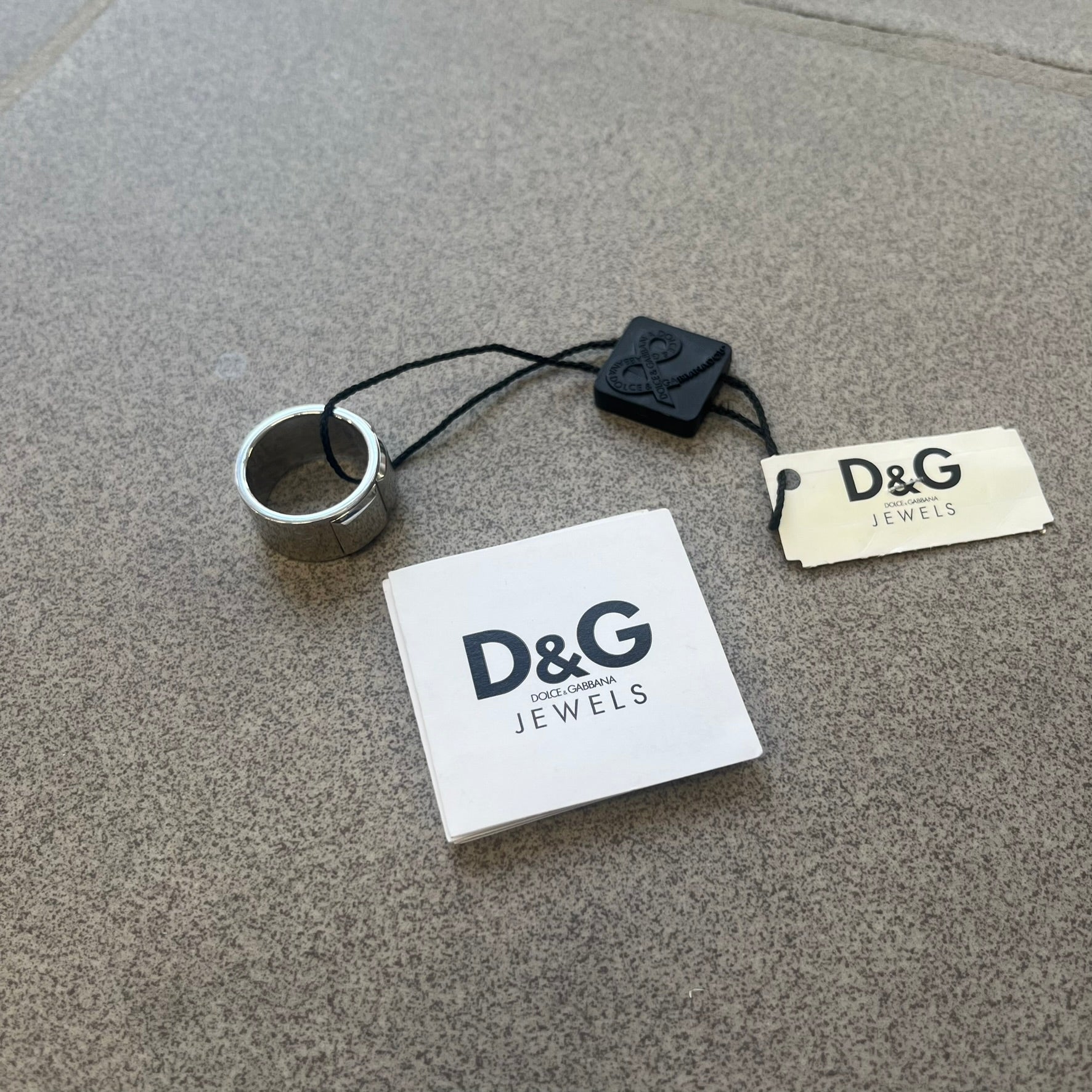 Dolce &amp; Gabbana DJ0836 Ring is made from silver-tone metal and features three raised square elements set across the top. Next to the squares, there is a small engraved D&amp;G logo. The ring has a clean, minimal design and is marked with model code DJ0836.