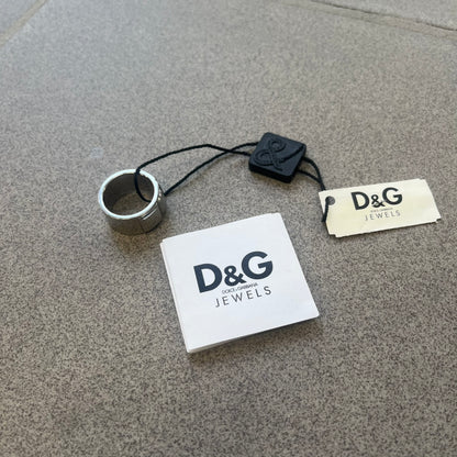 Dolce &amp; Gabbana DJ0836 Ring is made from silver-tone metal and features three raised square elements set across the top. Next to the squares, there is a small engraved D&amp;G logo. The ring has a clean, minimal design and is marked with model code DJ0836.