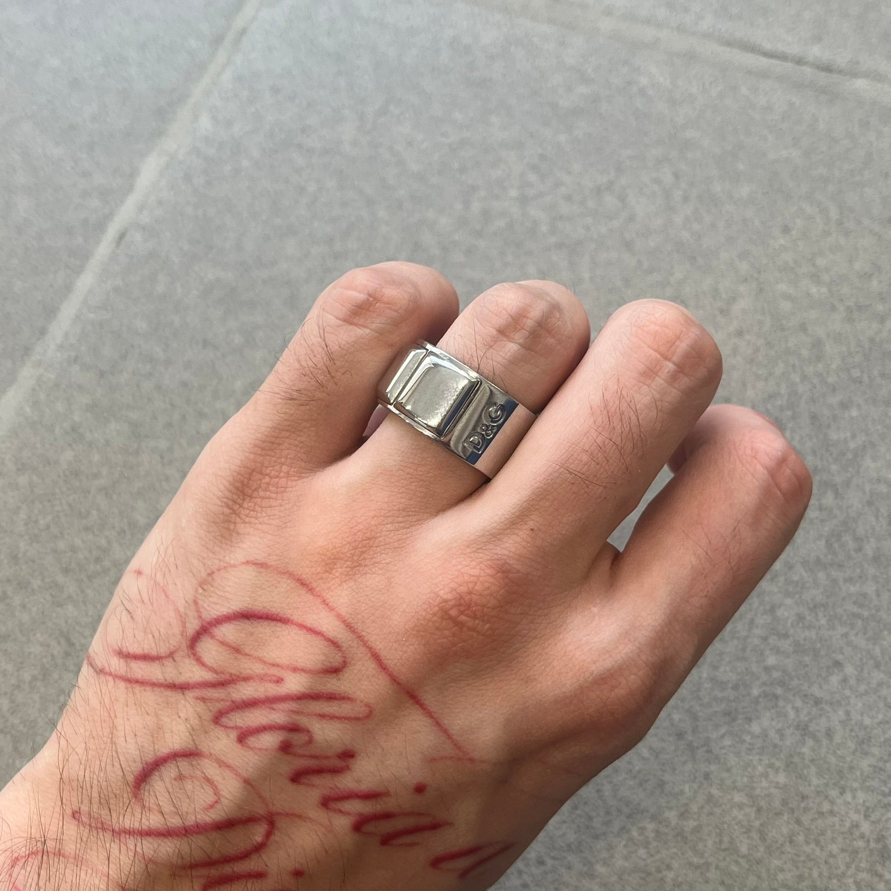 Dolce &amp; Gabbana DJ0836 Ring is made from silver-tone metal and features three raised square elements set across the top. Next to the squares, there is a small engraved D&amp;G logo. The ring has a clean, minimal design and is marked with model code DJ0836.