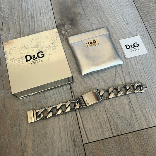 Dolce & Gabbana 2000’s Stainless Steel Bracelet DJ0552 is a thick bracelet made from stainless steel featuring large Cuban-style links. The center includes a plaque with a small engraved D&G logo, while the clasp is also marked with Dolce & Gabbana branding. The piece is referenced as DJ0552 and comes with the original box and dustbag.