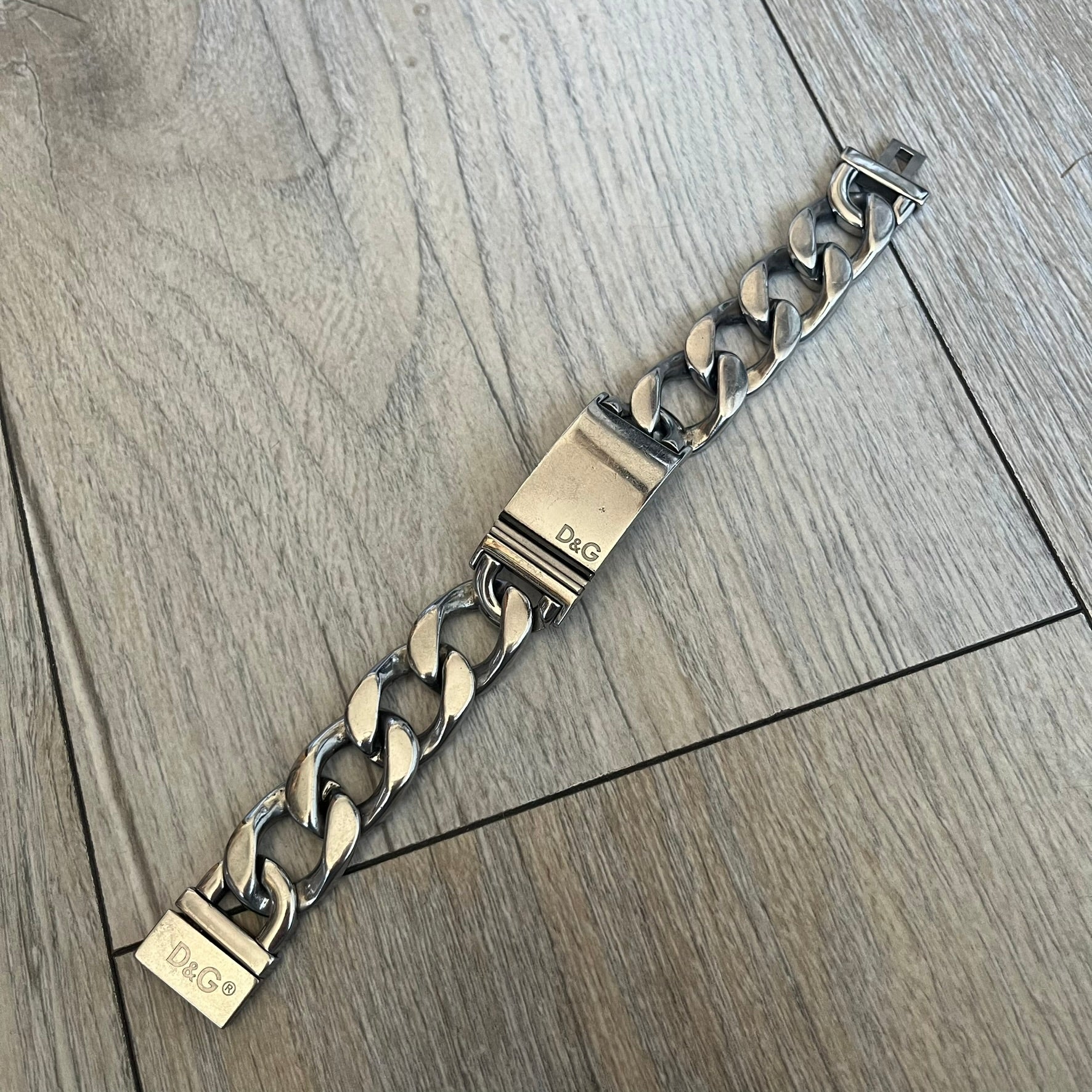 Dolce & Gabbana 2000’s Stainless Steel Bracelet DJ0552 is a thick bracelet made from stainless steel featuring large Cuban-style links. The center includes a plaque with a small engraved D&G logo, while the clasp is also marked with Dolce & Gabbana branding. The piece is referenced as DJ0552 and comes with the original box and dustbag.