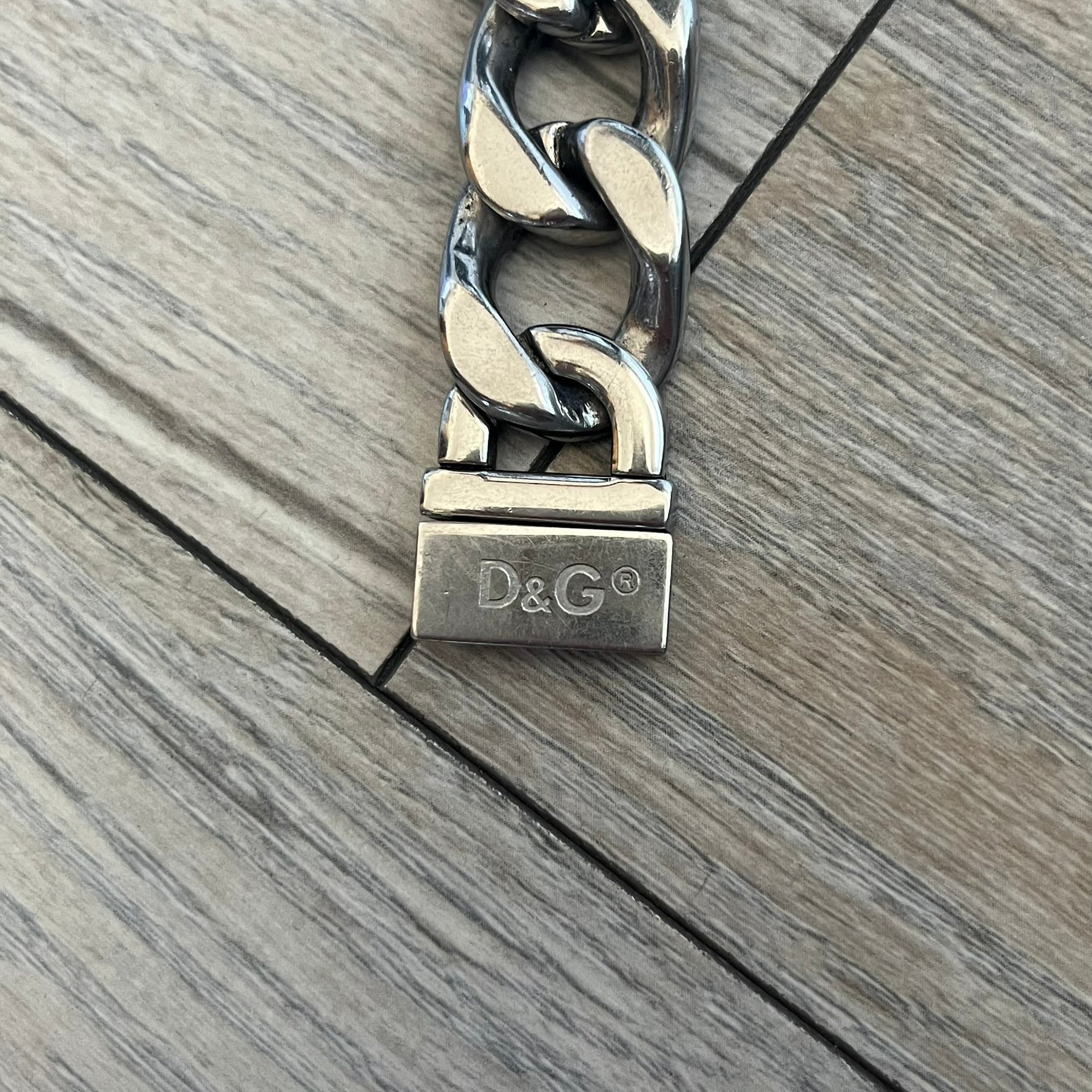 Dolce & Gabbana 2000’s Stainless Steel Bracelet DJ0552 is a thick bracelet made from stainless steel featuring large Cuban-style links. The center includes a plaque with a small engraved D&G logo, while the clasp is also marked with Dolce & Gabbana branding. The piece is referenced as DJ0552 and comes with the original box and dustbag.