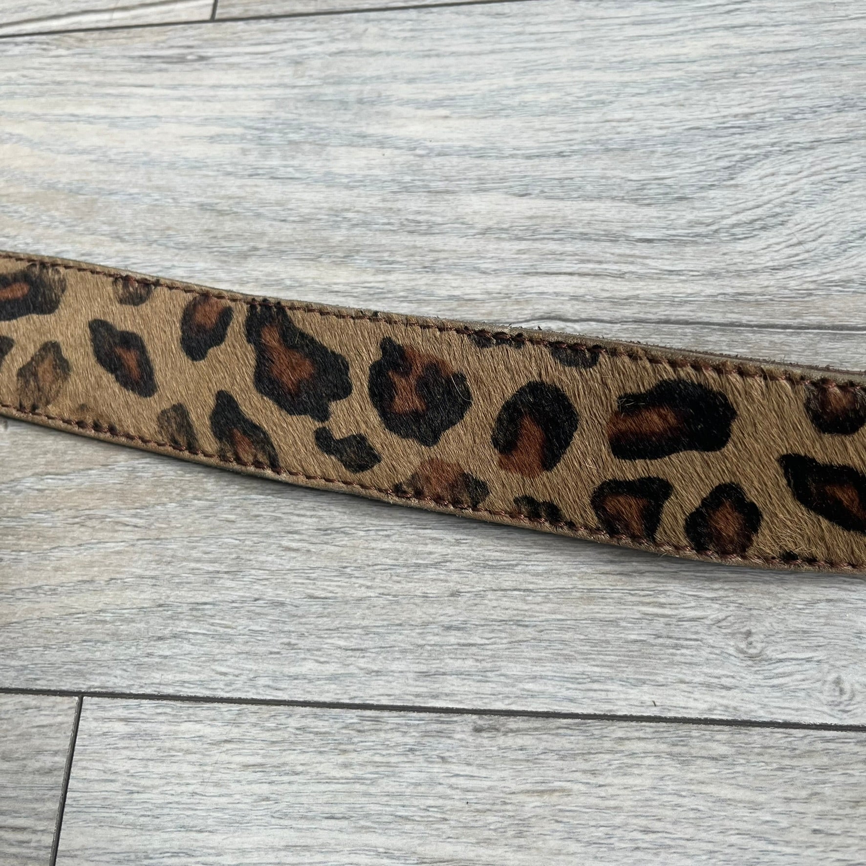 Dolce & Gabbana 2000s Studded Buckle Leopard Print Belt is a beige belt with an all-over leopard print and a short hair-textured exterior. The buckle features an italic-style D&G logo in a silver-tone finish with rhinestone detailing. The interior is finished in brown leather.