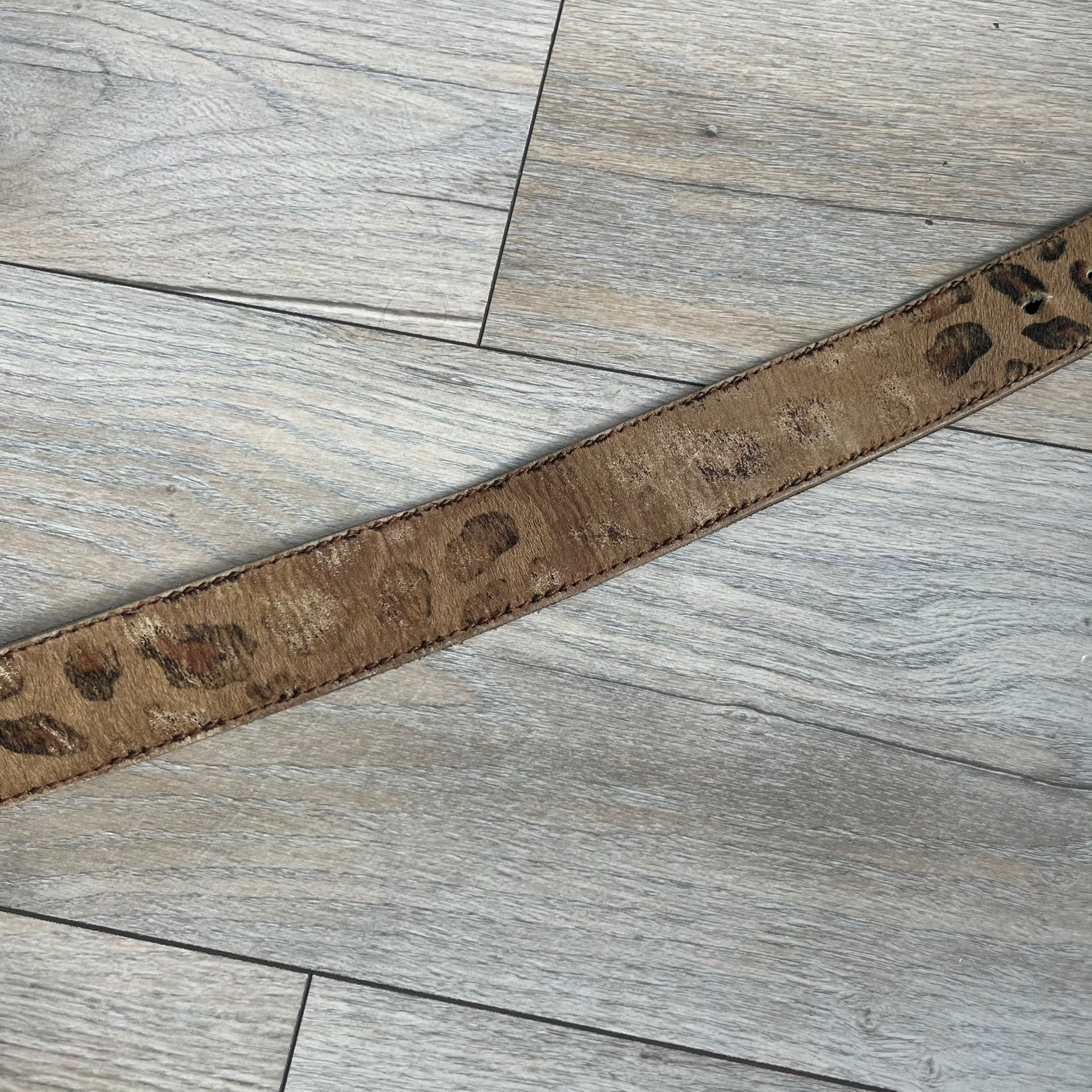 Dolce & Gabbana 2000s Studded Buckle Leopard Print Belt is a beige belt with an all-over leopard print and a short hair-textured exterior. The buckle features an italic-style D&G logo in a silver-tone finish with rhinestone detailing. The interior is finished in brown leather.