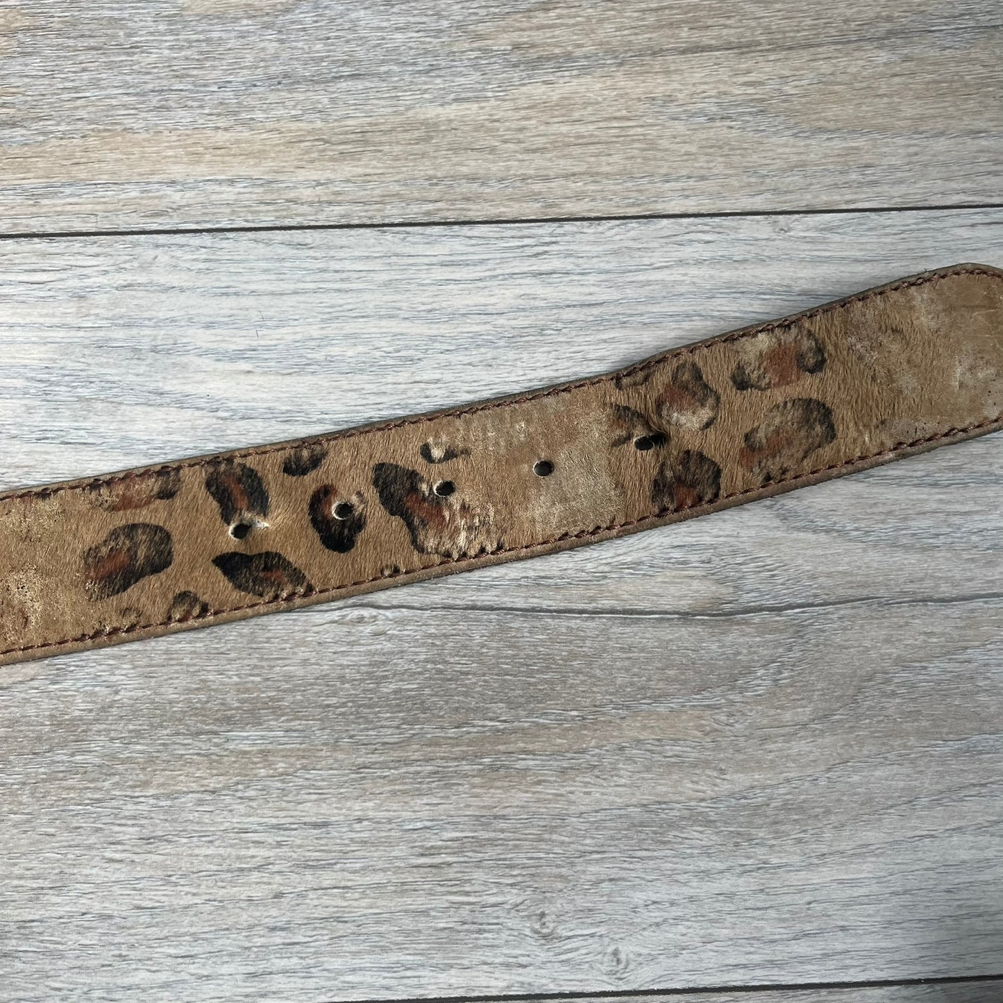 Dolce & Gabbana 2000s Studded Buckle Leopard Print Belt is a beige belt with an all-over leopard print and a short hair-textured exterior. The buckle features an italic-style D&G logo in a silver-tone finish with rhinestone detailing. The interior is finished in brown leather.