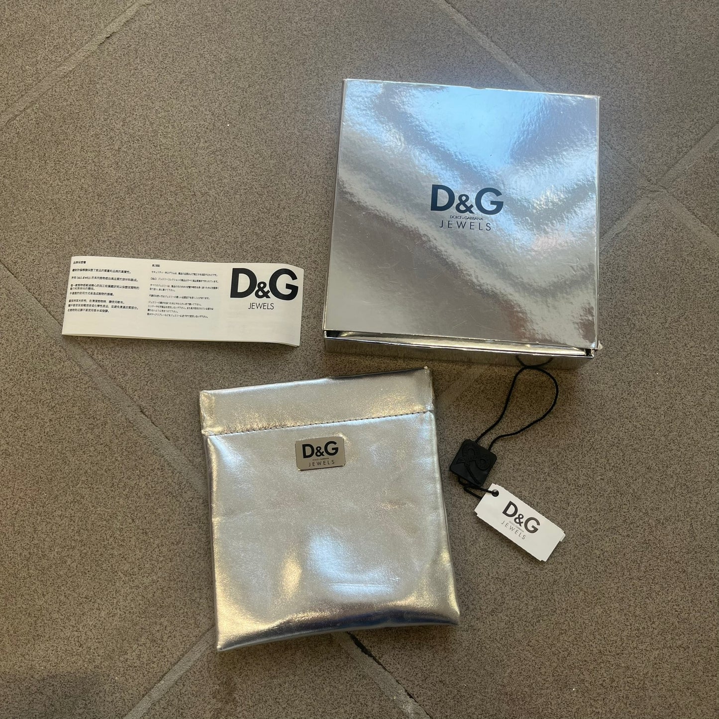Dolce &amp; Gabbana 2000s "Training Sport System" Bracelet (DJ0455) is a wide brown leather bracelet featuring a stainless steel plaque at the center. The plaque is detailed with a raised D&amp;G logo, "Training Sport System" text and "94" graphics set against red and navy backgrounds. The interior is stamped with D&amp;G branding and "Genuine Leather" markings. The bracelet fastens with two snap-button size adjustments and comes complete with its original box, dust bag, and papers.