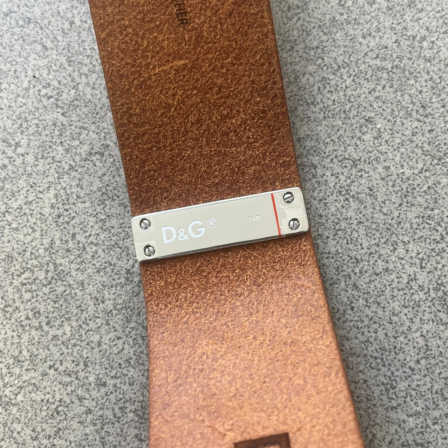 Dolce & Gabbana 2000s "Training Sport System" Bracelet (DJ0455) is a wide brown leather bracelet featuring a stainless steel plaque at the center. The plaque is detailed with a raised D&G logo, "Training Sport System" text, "94," and "3" graphics set against red and navy backgrounds. The interior is stamped with D&G branding and "Genuine Leather" markings. The bracelet fastens with two snap-button size adjustments and comes complete with its original box, dust bag, and papers.
