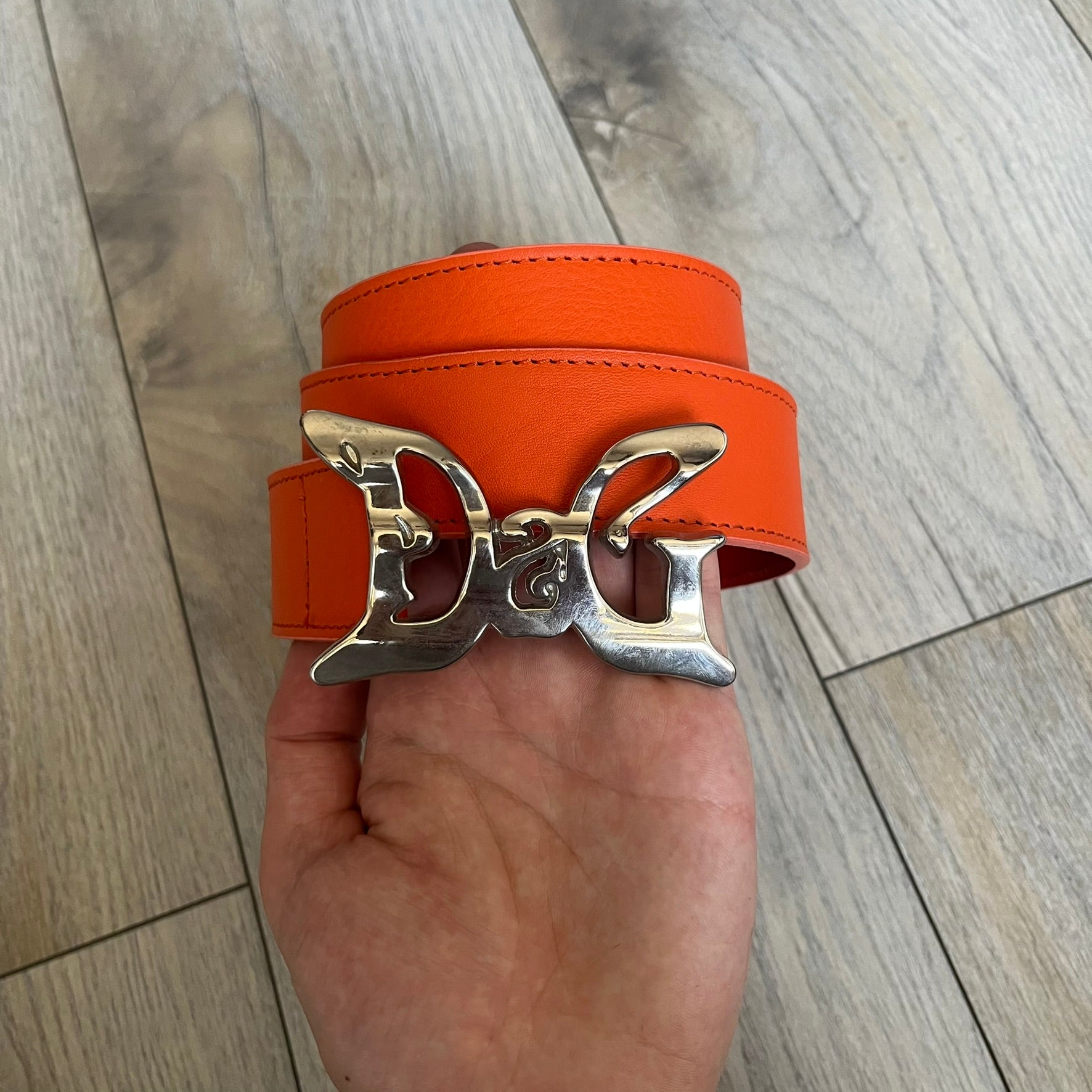 Dolce &amp; Gabbana 2008 Butterfly Buckle Orange Leather Belt from the AW2008 collection. Crafted from smooth orange leather with visible edge stitching, this belt features a big silver-tone D&amp;G logo buckle shaped in a butterfly-style form. The buckle has a polished metal finish, while the belt itself is made from 100% leather and retains a clean, structured profile. An original seasonal accessory from Dolce &amp; Gabbana’s AW2008 season.