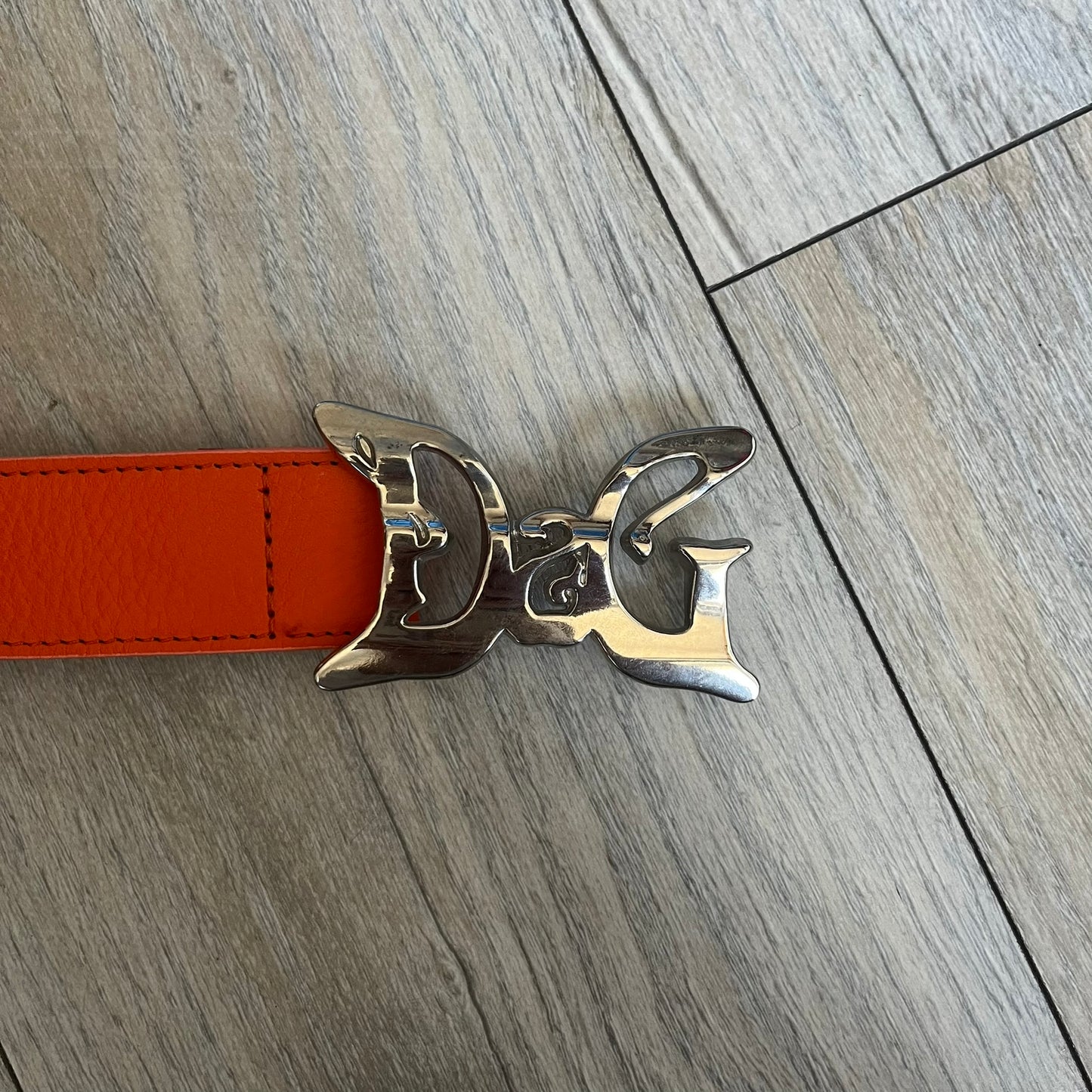 Dolce &amp; Gabbana 2008 Butterfly Buckle Orange Leather Belt from the AW2008 collection. Crafted from smooth orange leather with visible edge stitching, this belt features a big silver-tone D&amp;G logo buckle shaped in a butterfly-style form. The buckle has a polished metal finish, while the belt itself is made from 100% leather and retains a clean, structured profile. An original seasonal accessory from Dolce &amp; Gabbana’s AW2008 season.