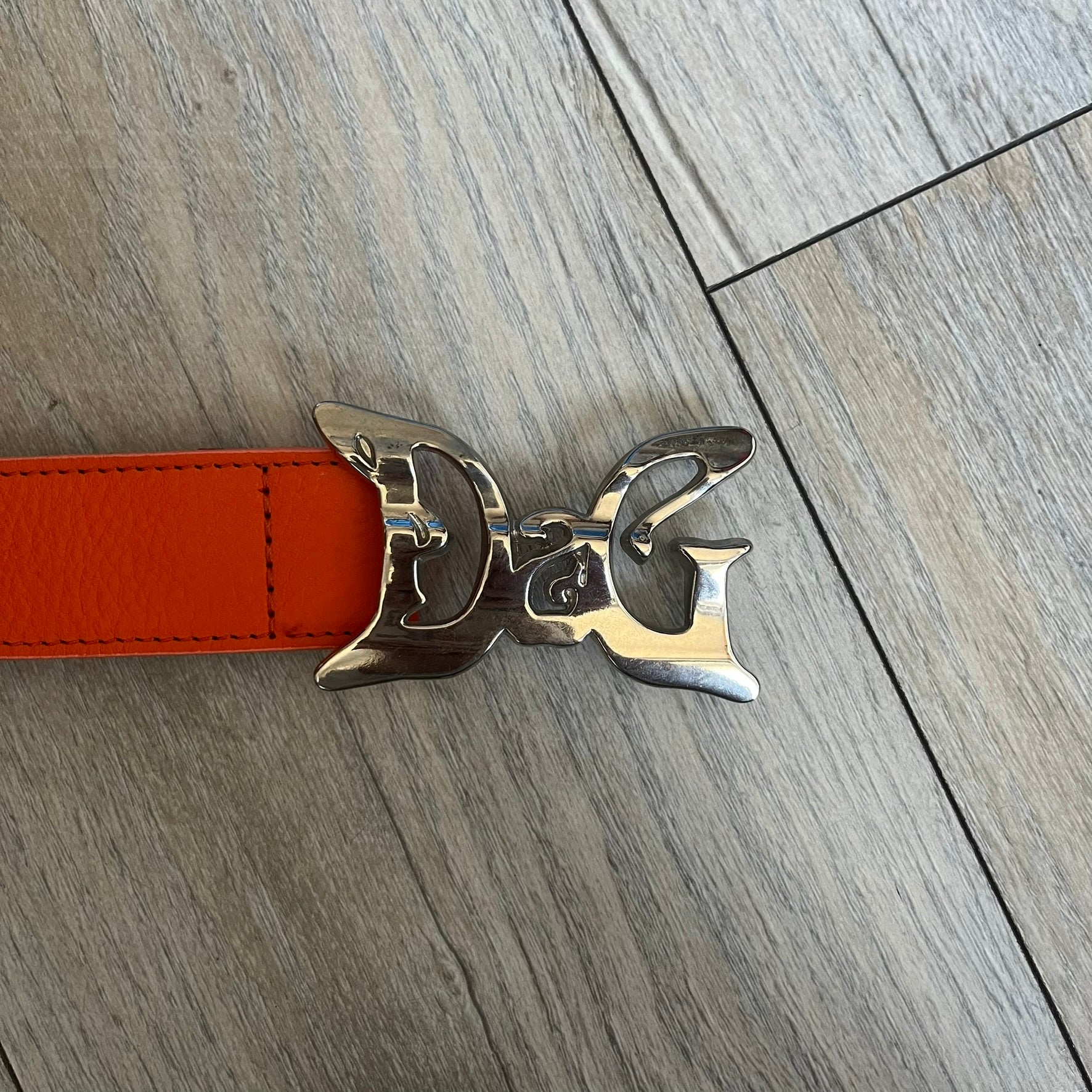 Dolce &amp; Gabbana 2008 Butterfly Buckle Orange Leather Belt from the AW2008 collection. Crafted from smooth orange leather with visible edge stitching, this belt features a big silver-tone D&amp;G logo buckle shaped in a butterfly-style form. The buckle has a polished metal finish, while the belt itself is made from 100% leather and retains a clean, structured profile. An original seasonal accessory from Dolce &amp; Gabbana’s AW2008 season.