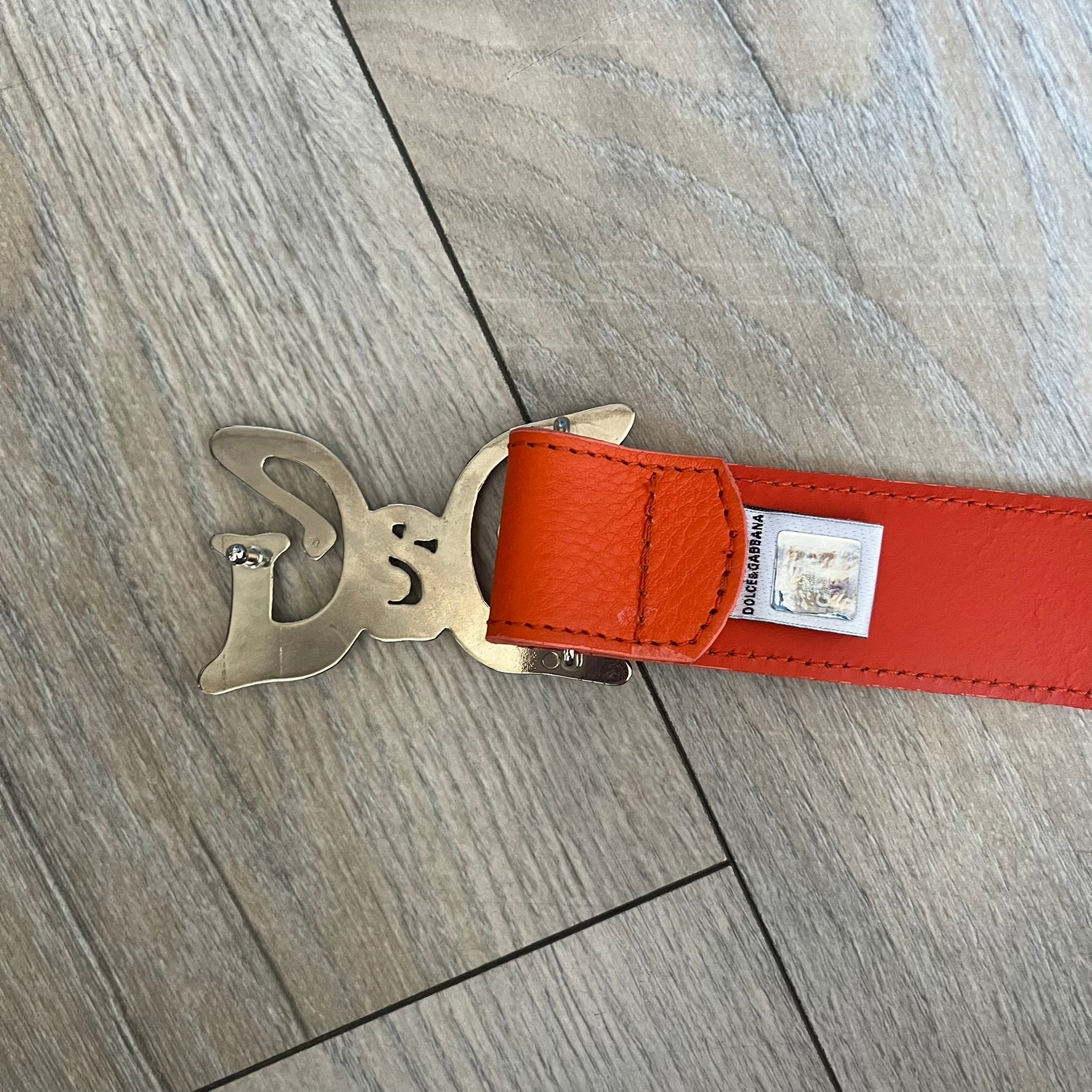 Dolce &amp; Gabbana 2008 Butterfly Buckle Orange Leather Belt from the AW2008 collection. Crafted from smooth orange leather with visible edge stitching, this belt features a big silver-tone D&amp;G logo buckle shaped in a butterfly-style form. The buckle has a polished metal finish, while the belt itself is made from 100% leather and retains a clean, structured profile. An original seasonal accessory from Dolce &amp; Gabbana’s AW2008 season.