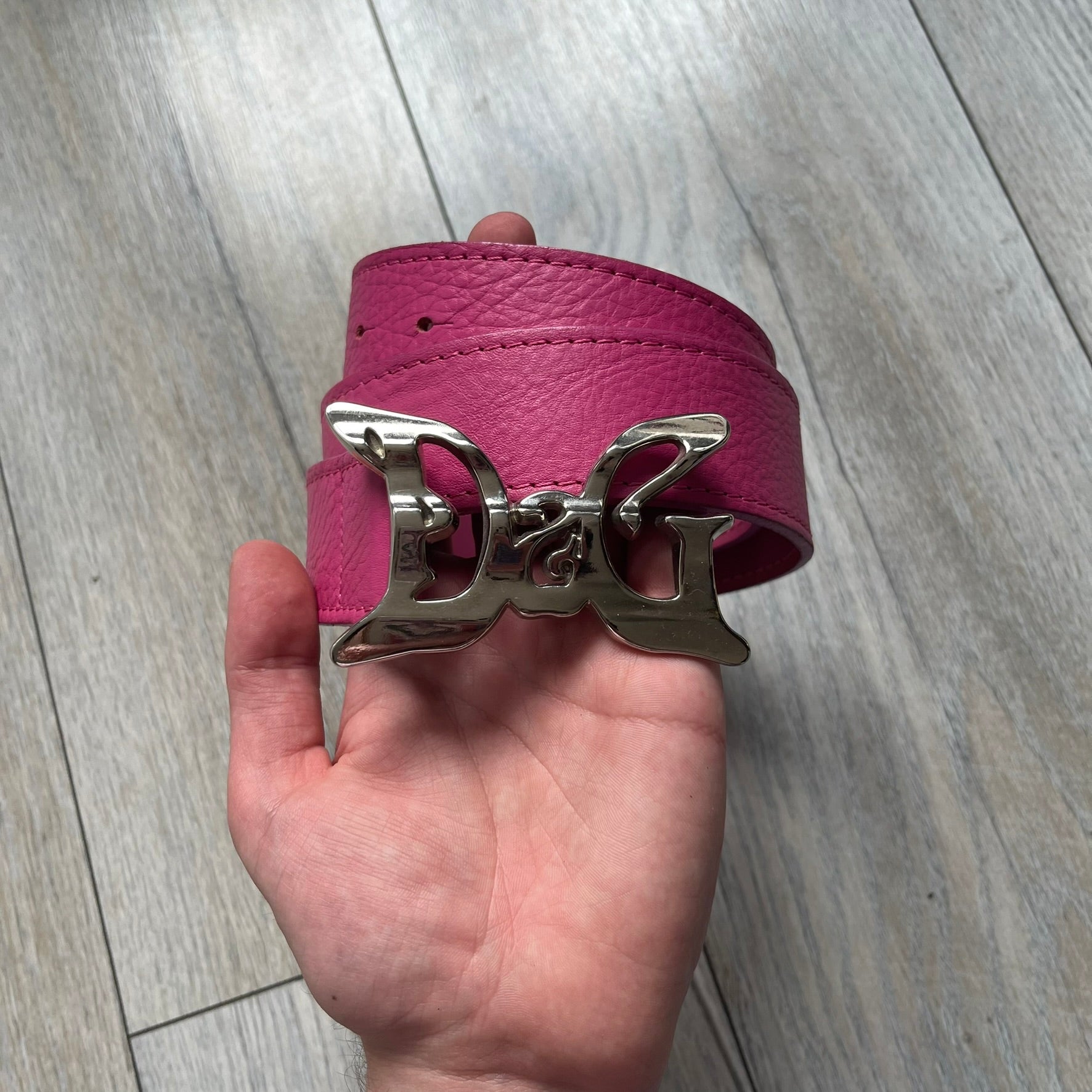 Dolce &amp; Gabbana 2008 Butterfly Buckle Pink Leather Belt from the AW2008 collection. Crafted from smooth pink leather with visible edge stitching, this belt features a big silver-tone D&amp;G logo buckle shaped in a butterfly-style form. The buckle has a polished metal finish, while the belt itself is made from 100% leather and retains a clean, structured profile. An original seasonal accessory from Dolce &amp; Gabbana’s AW2008 season.