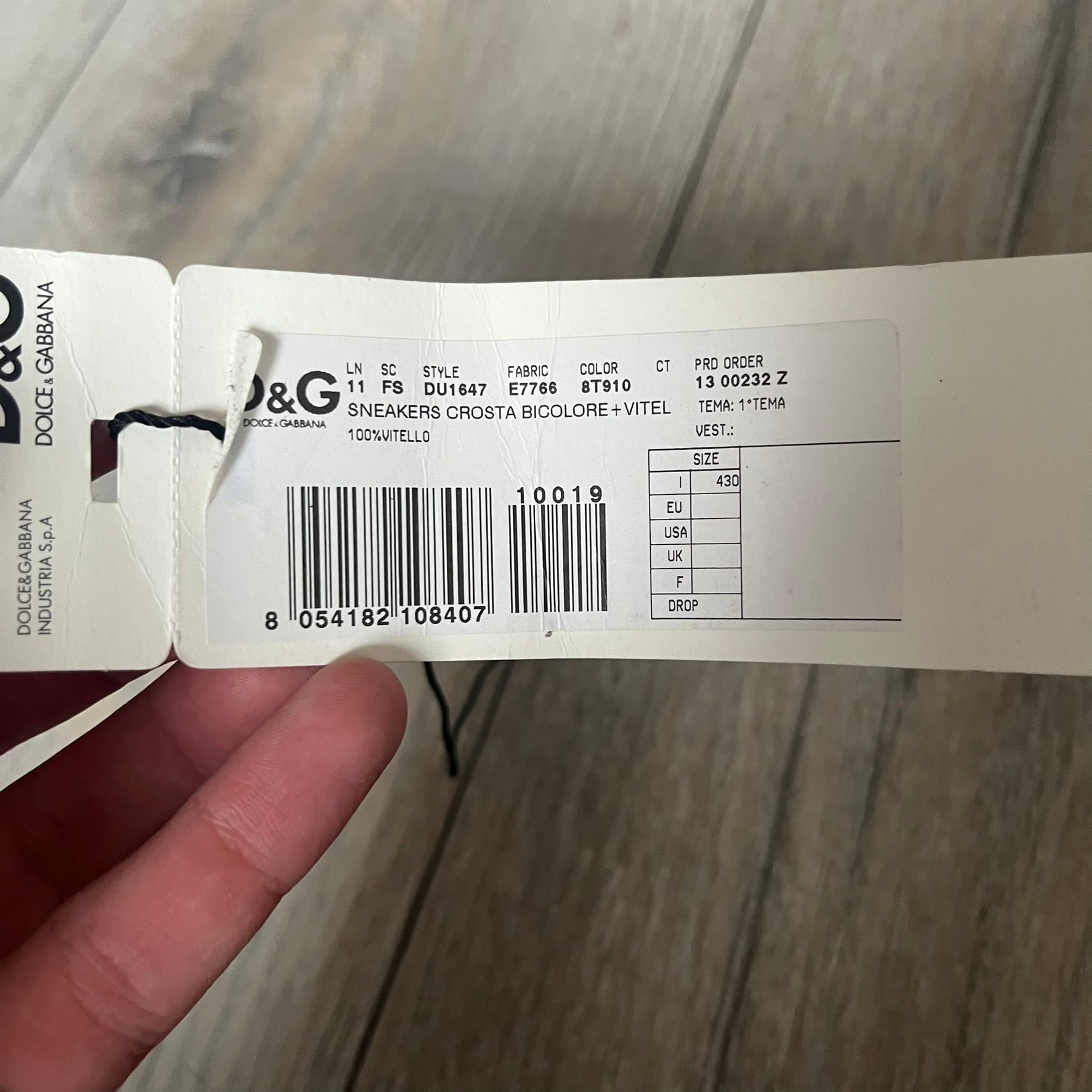 Dolce & Gabbana 2013 Bicolor Sneakers are black leather sneakers with a brown rubber sole. They feature red leather stripes on the sides, tongue details, and a back stripe, with black D&G logos on the sides and tongue. The sneakers come with the original box and tags.