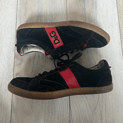 Dolce & Gabbana 2013 Bicolor Sneakers are black leather sneakers with a brown rubber sole. They feature red leather stripes on the sides, tongue details, and a back stripe, with black D&G logos on the sides and tongue. The sneakers come with the original box and tags.