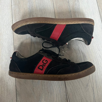 Dolce & Gabbana 2013 Bicolor Sneakers are black leather sneakers with a brown rubber sole. They feature red leather stripes on the sides, tongue details, and a back stripe, with black D&G logos on the sides and tongue. The sneakers come with the original box and tags.