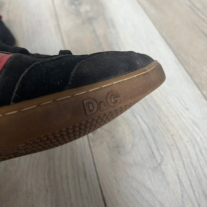 Dolce & Gabbana 2013 Bicolor Sneakers are black leather sneakers with a brown rubber sole. They feature red leather stripes on the sides, tongue details, and a back stripe, with black D&G logos on the sides and tongue. The sneakers come with the original box and tags.