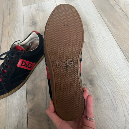 Dolce & Gabbana 2013 Bicolor Sneakers are black leather sneakers with a brown rubber sole. They feature red leather stripes on the sides, tongue details, and a back stripe, with black D&G logos on the sides and tongue. The sneakers come with the original box and tags.