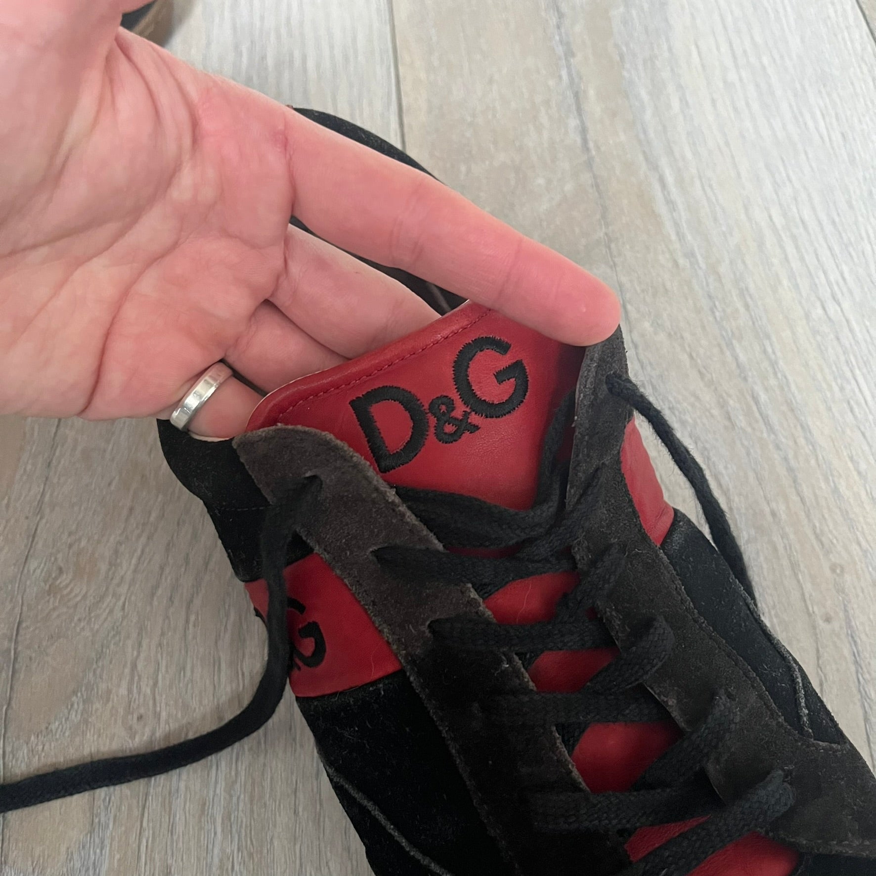 Dolce & Gabbana 2013 Bicolor Sneakers are black leather sneakers with a brown rubber sole. They feature red leather stripes on the sides, tongue details, and a back stripe, with black D&G logos on the sides and tongue. The sneakers come with the original box and tags.