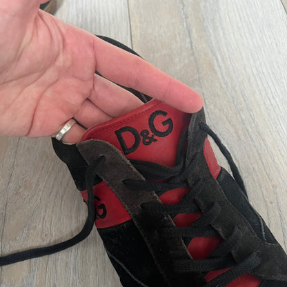 Dolce & Gabbana 2013 Bicolor Sneakers are black leather sneakers with a brown rubber sole. They feature red leather stripes on the sides, tongue details, and a back stripe, with black D&G logos on the sides and tongue. The sneakers come with the original box and tags.