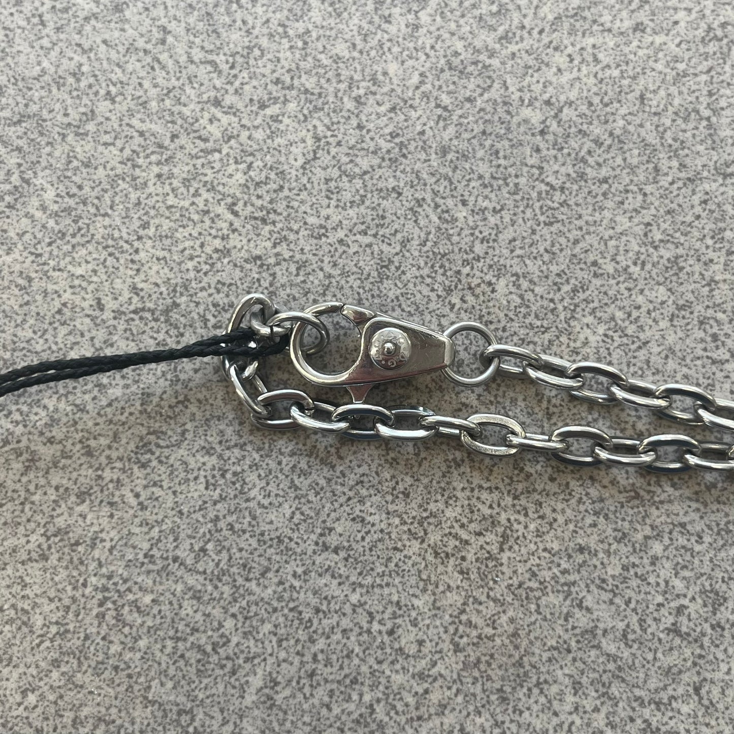 The Dolce &amp; Gabbana Star Dog Tag Necklace (DJ0889) is a heavy stainless steel necklace featuring a thick, oversized dog tag pendant. The front of the pendant has a raised black star mounted on a silver-tone circular base, with open cutout sections between the star and the circle. A raised D&amp;G logo is positioned at the lower front of the dog tag. The necklace is finished with a lobster clasp and has a solid, weighty construction throughout.