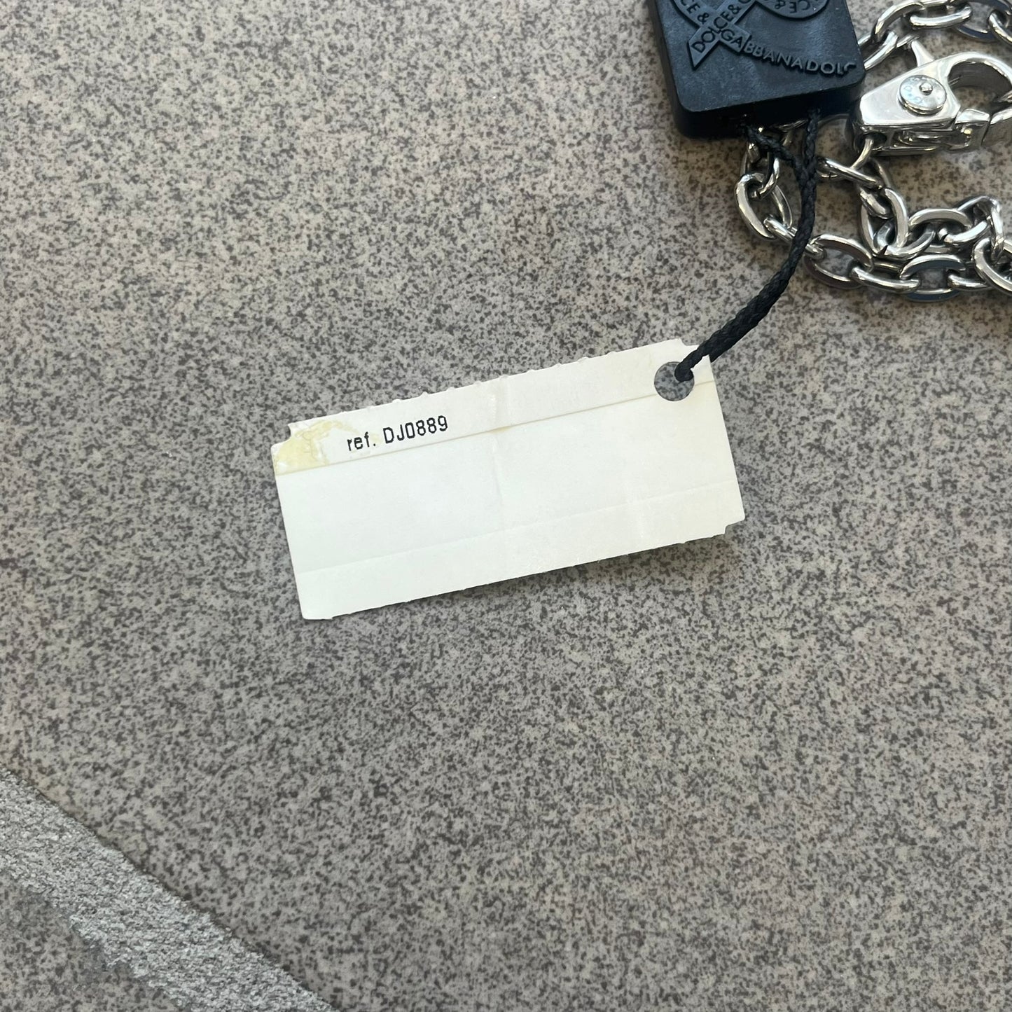 The Dolce &amp; Gabbana Star Dog Tag Necklace (DJ0889) is a heavy stainless steel necklace featuring a thick, oversized dog tag pendant. The front of the pendant has a raised black star mounted on a silver-tone circular base, with open cutout sections between the star and the circle. A raised D&amp;G logo is positioned at the lower front of the dog tag. The necklace is finished with a lobster clasp and has a solid, weighty construction throughout.