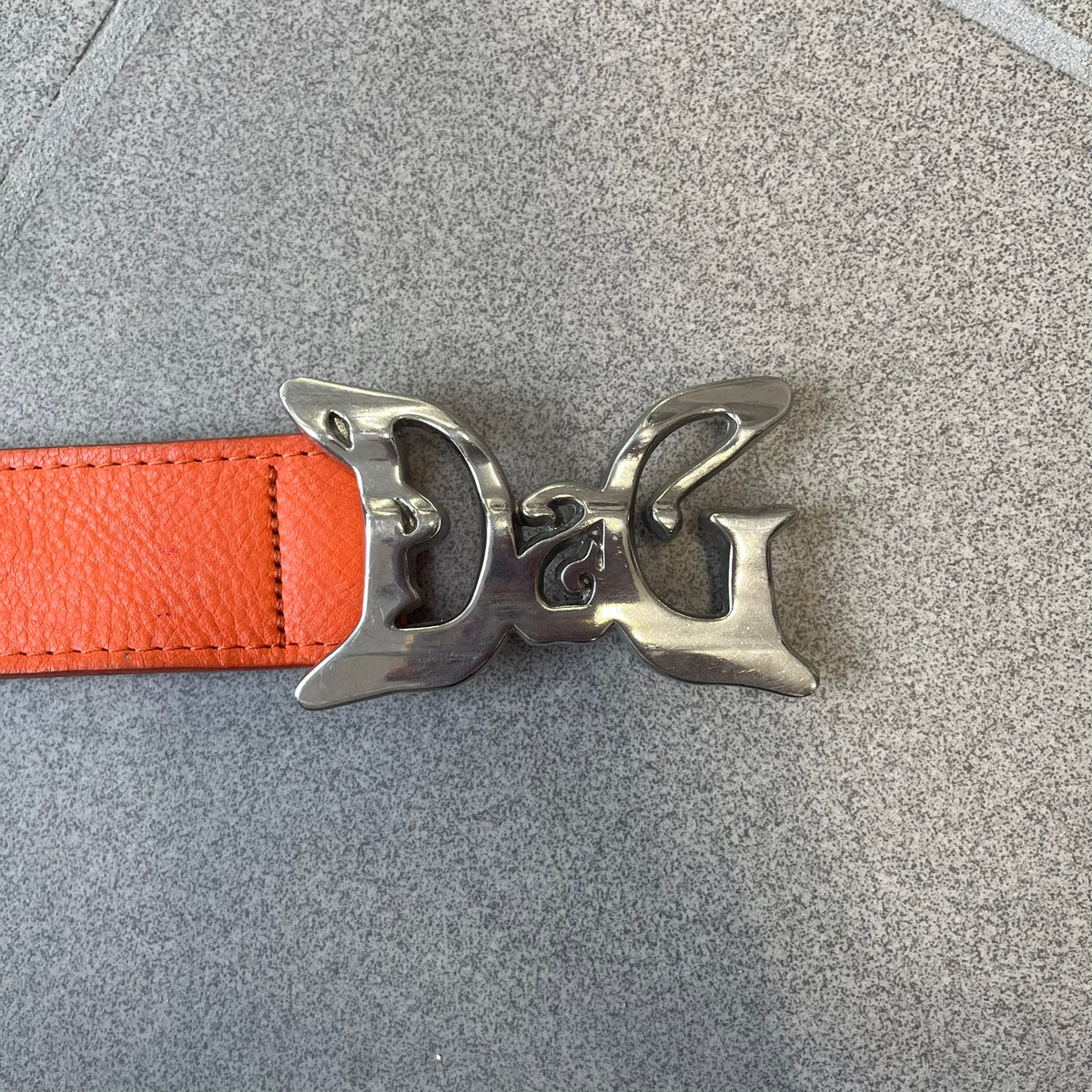 Dolce &amp; Gabbana 2008 Butterfly Buckle Orange Leather Belt from the AW2008 collection. Crafted from smooth orange leather with visible edge stitching, this belt features a big silver-tone D&amp;G logo buckle shaped in a butterfly-style form. The buckle has a polished metal finish, while the belt itself is made from 100% leather and retains a clean, structured profile. An original seasonal accessory from Dolce &amp; Gabbana’s AW2008 season.