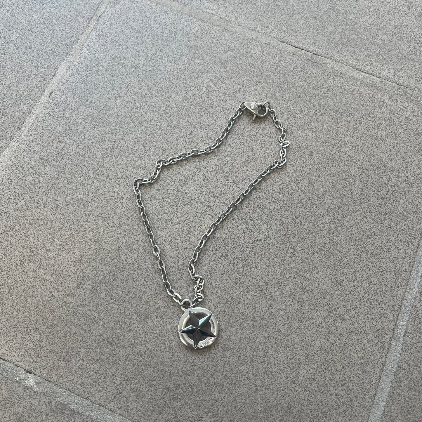 Dolce &amp; Gabbana AW2009 Military Star Necklace in grey. Features a 3D black star mounted on a silver-tone metal circle with an engraved D&amp;G logo at the bottom, suspended from a silver cable chain. Lobster clasp with small D&amp;G markings.