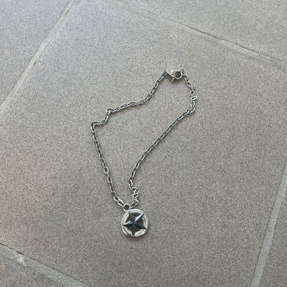 Dolce &amp; Gabbana AW2009 Military Star Necklace in grey. Features a 3D black star mounted on a silver-tone metal circle with an engraved D&amp;G logo at the bottom, suspended from a silver cable chain. Lobster clasp with small D&amp;G markings.