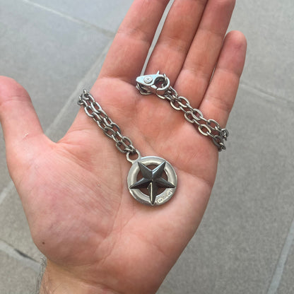 Dolce &amp; Gabbana AW2009 Military Star Necklace in grey. Features a 3D black star mounted on a silver-tone metal circle with an engraved D&amp;G logo at the bottom, suspended from a silver cable chain. Lobster clasp with small D&amp;G markings.