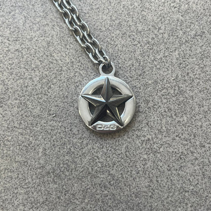 Dolce &amp; Gabbana AW2009 Military Star Necklace in grey. Features a 3D black star mounted on a silver-tone metal circle with an engraved D&amp;G logo at the bottom, suspended from a silver cable chain. Lobster clasp with small D&amp;G markings.