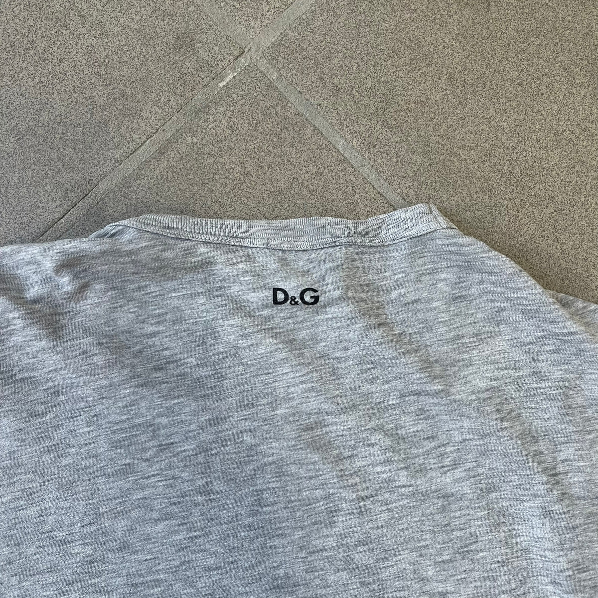 Dolce & Gabbana AW2011 Coca Cola Tee is a gray T-shirt made in collaboration with Coca-Cola, featuring a vintage promo-style graphic on the front of a six-pack of Coca-Cola bottles with “Introducing our new plastic carrier” text. It has licensed tags and a small black D&G logo on the upper back.