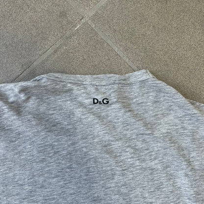 Dolce & Gabbana AW2011 Coca Cola Tee is a gray T-shirt made in collaboration with Coca-Cola, featuring a vintage promo-style graphic on the front of a six-pack of Coca-Cola bottles with “Introducing our new plastic carrier” text. It has licensed tags and a small black D&G logo on the upper back.