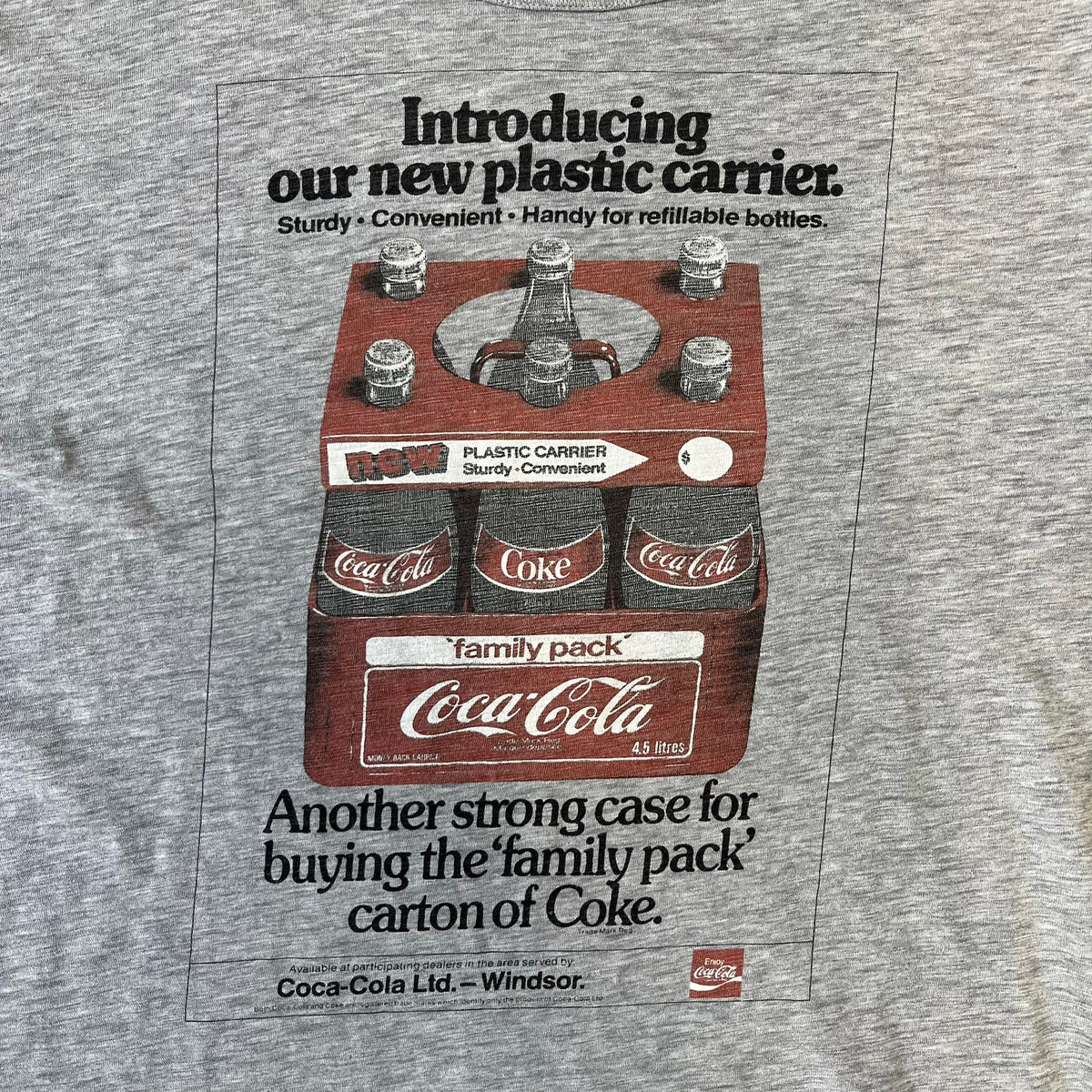 Dolce & Gabbana AW2011 Coca Cola Tee is a gray T-shirt made in collaboration with Coca-Cola, featuring a vintage promo-style graphic on the front of a six-pack of Coca-Cola bottles with “Introducing our new plastic carrier” text. It has licensed tags and a small black D&G logo on the upper back.
