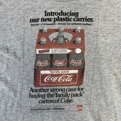Dolce & Gabbana AW2011 Coca Cola Tee is a gray T-shirt made in collaboration with Coca-Cola, featuring a vintage promo-style graphic on the front of a six-pack of Coca-Cola bottles with “Introducing our new plastic carrier” text. It has licensed tags and a small black D&G logo on the upper back.