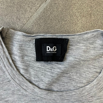 Dolce & Gabbana AW2011 Coca Cola Tee is a gray T-shirt made in collaboration with Coca-Cola, featuring a vintage promo-style graphic on the front of a six-pack of Coca-Cola bottles with “Introducing our new plastic carrier” text. It has licensed tags and a small black D&G logo on the upper back.