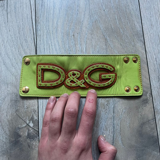 The Dolce &amp; Gabbana Big Green Leather Bracelet is a tall green leather wristband featuring a layered D&amp;G logo along its length - an orange base layer with a green logo on top, detailed with visible orange stitching. The inside has a Dolce &amp; Gabbana tag, and it closes with two metal buttons, offering four total button positions for adjustable sizing.