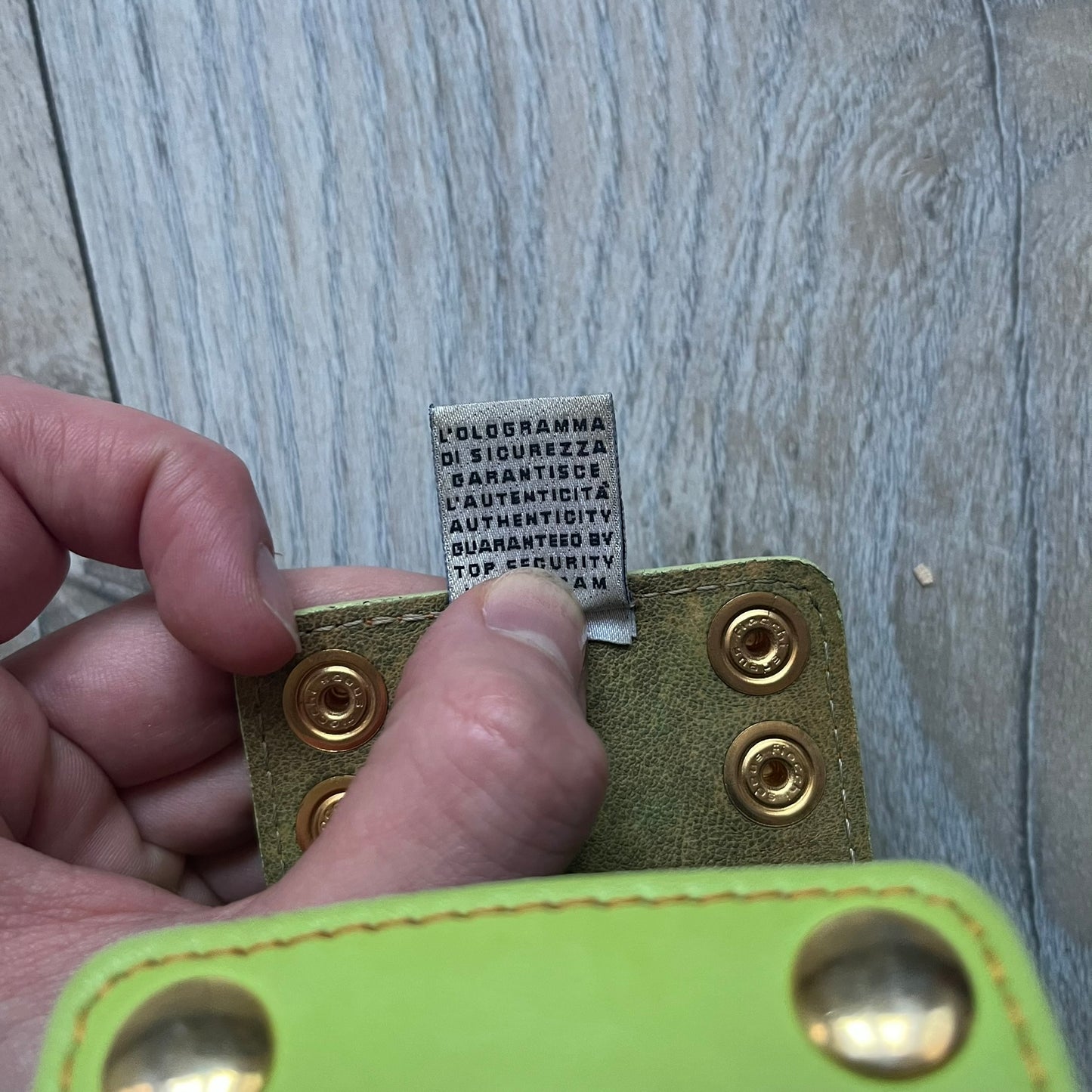 The Dolce &amp; Gabbana Big Green Leather Bracelet is a tall green leather wristband featuring a layered D&amp;G logo along its length - an orange base layer with a green logo on top, detailed with visible orange stitching. The inside has a Dolce &amp; Gabbana tag, and it closes with two metal buttons, offering four total button positions for adjustable sizing.